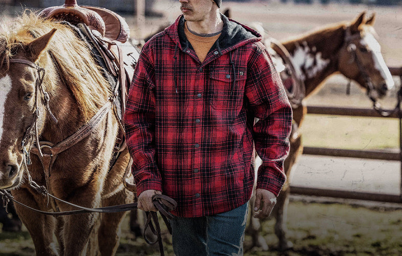 man in flannel jacket standing by two horses in fenced area